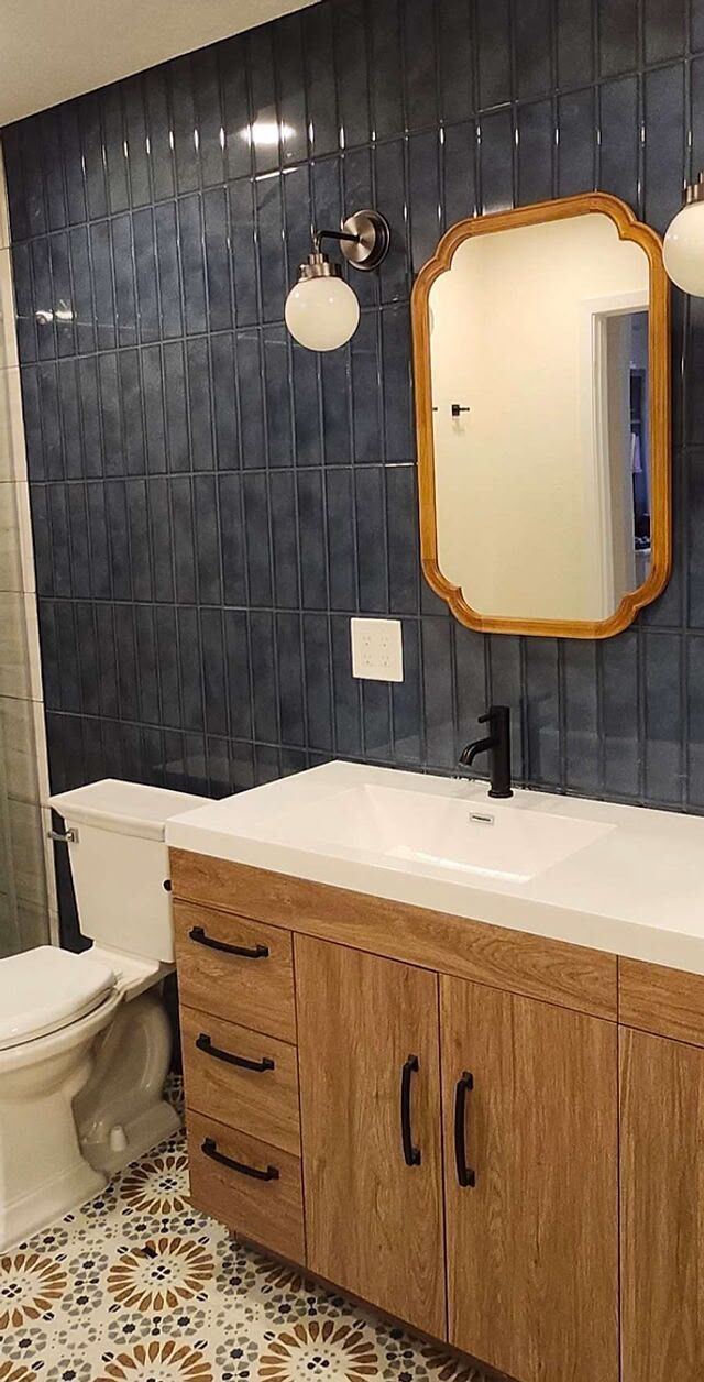 Bathroom with a stacked blue tile accent wall, wood vanity and globe sconces